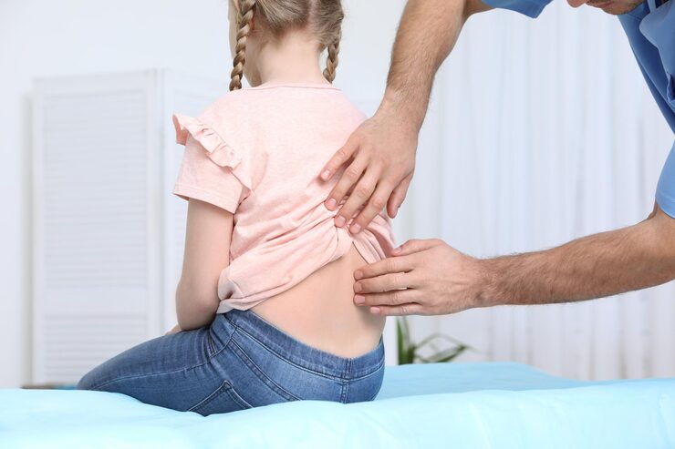 Child receiving chiropractic examination for scoliosis treatment, chiropractor assessing spinal alignment in a clinical setting.