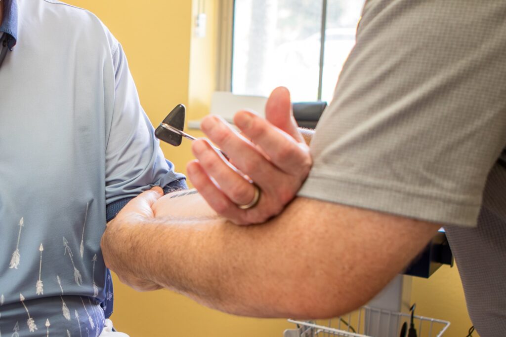 Close-up of Dr. Michael Cox examining a patient's elbow with a reflex hammer at Insight Chiropractic in Ormond Beach