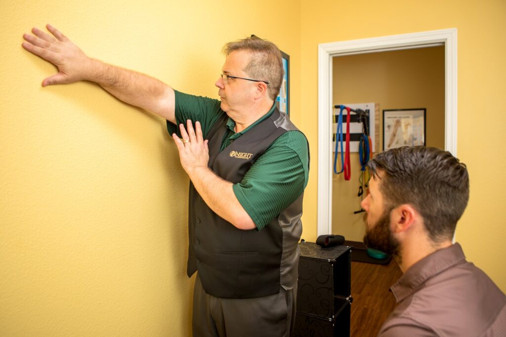 Dr. Michael Cox demonstrating a wall stretch for a patient at Insight Chiropractic