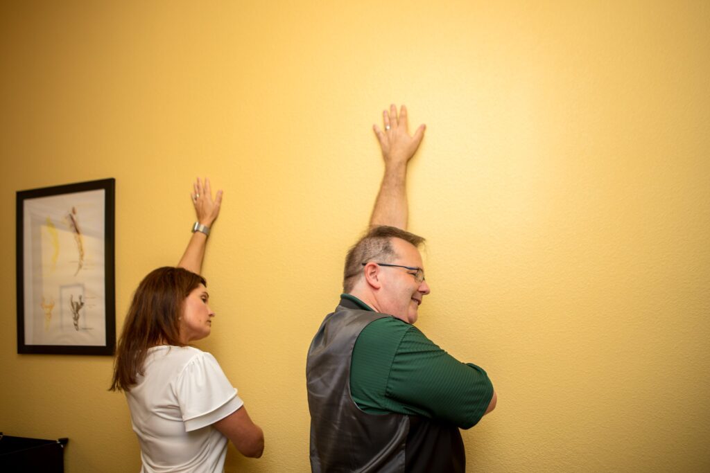 Dr. Michael Cox checking a patient's overhead shoulder range of motion against the wall at Insight Chiropractic
